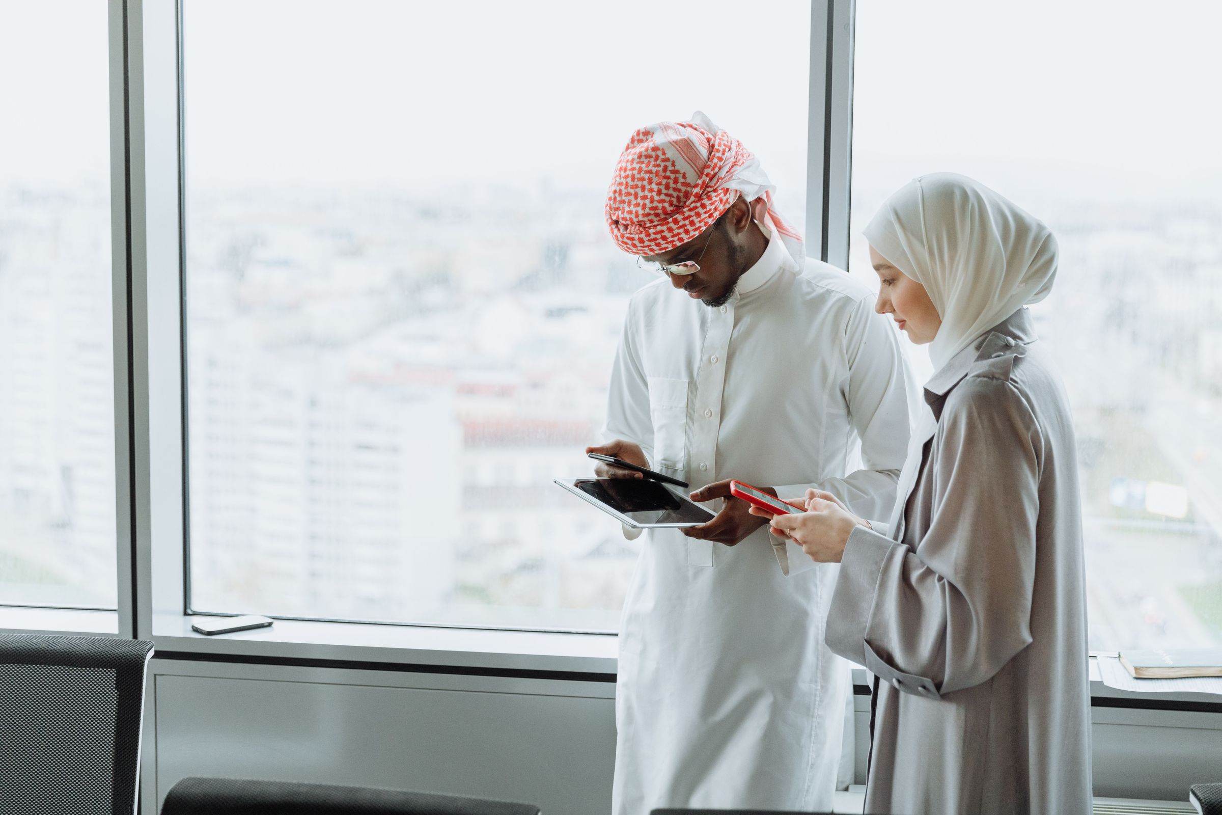 Two colleagues in a Gulf office reviewing figures on a tablet and a phone
